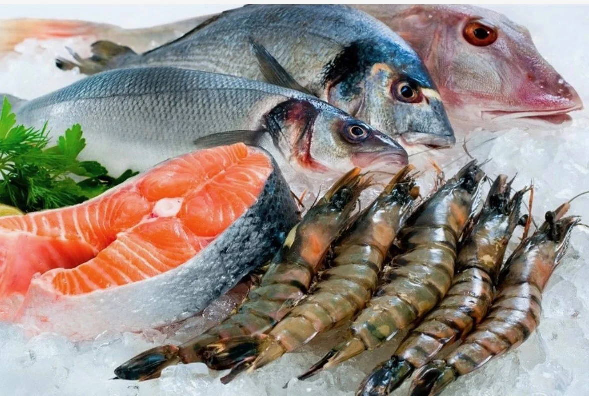 Whole fish, a salmon steak and raw black tiger prawns arranged on crushed ice with parsley